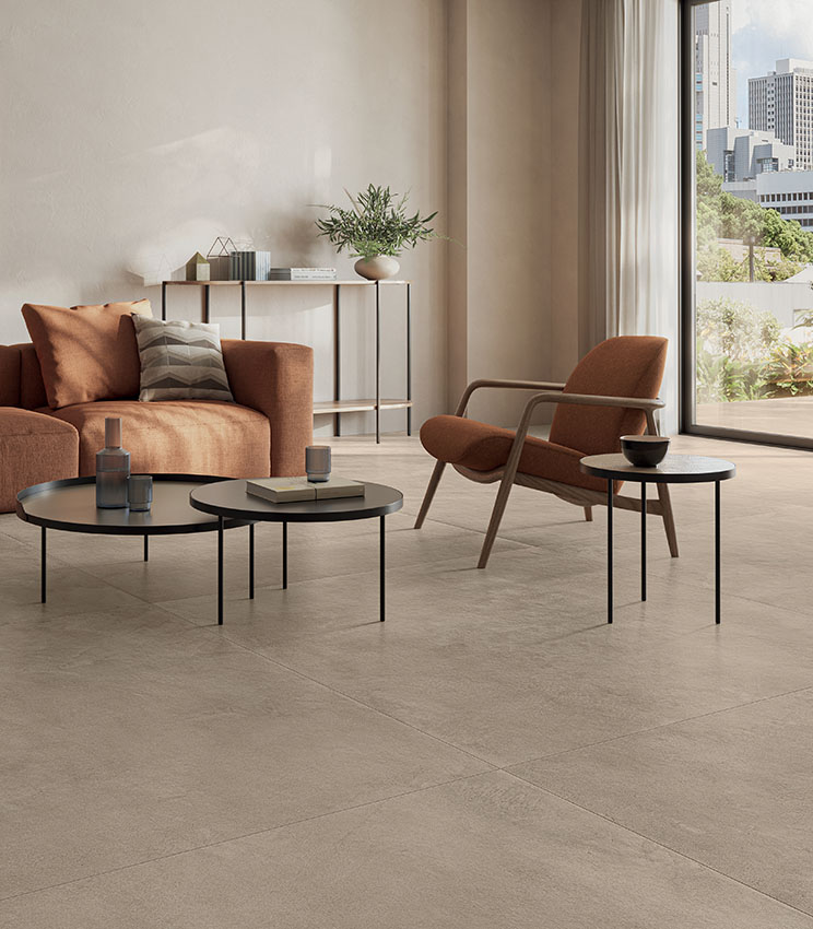 Moderno living dai toni caldi e terrosi, con portafinestra su terrazzo e pavimento in gres porcellanato effetto cemento color sabbia.