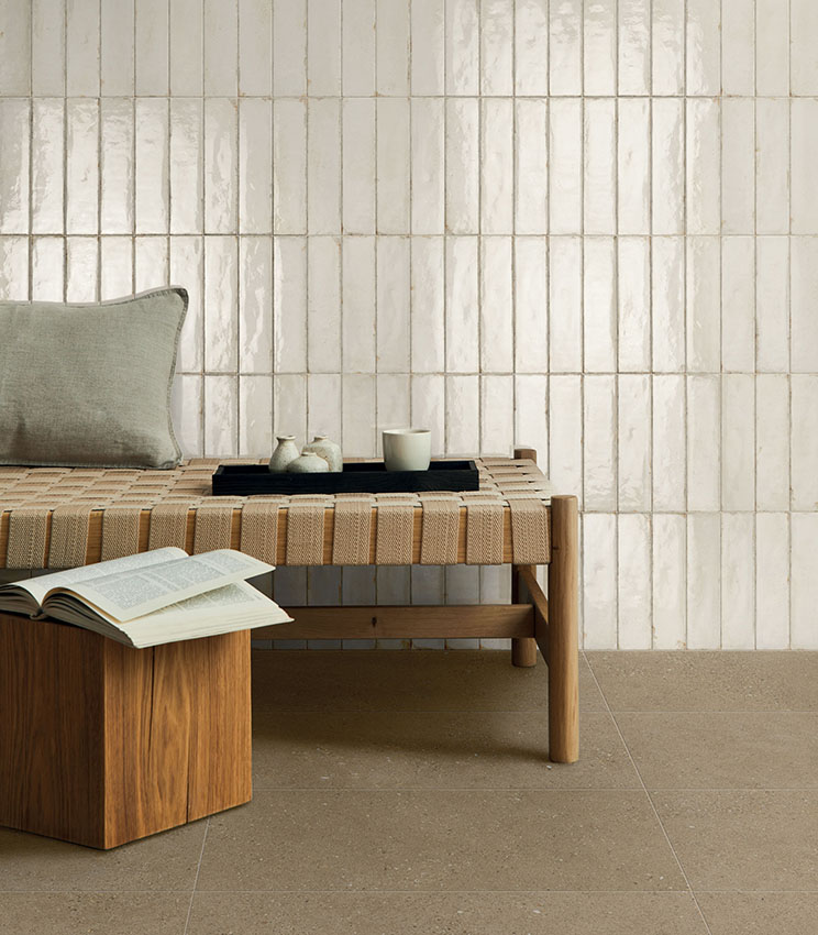 Ambiente moderno e rilassante con panca in legno e seduta intrecciata, parete rivestita con piastrelle ceramiche lucide color avorio e pavimento in gres porcellanato dai toni naturali.