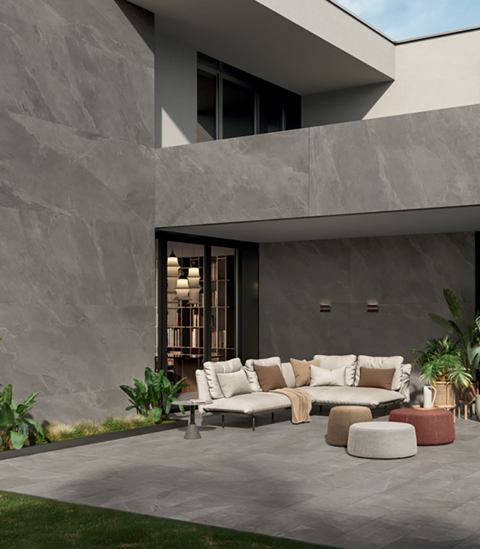 Veduta esterna di villa dal design moderno e rigorosamente geometrico, parzialmente rivestita con grandi lastre ceramiche effetto pietra, con patio arredato pavimentato con gres porcellanato effetto pietra in 20 mm di spessore.