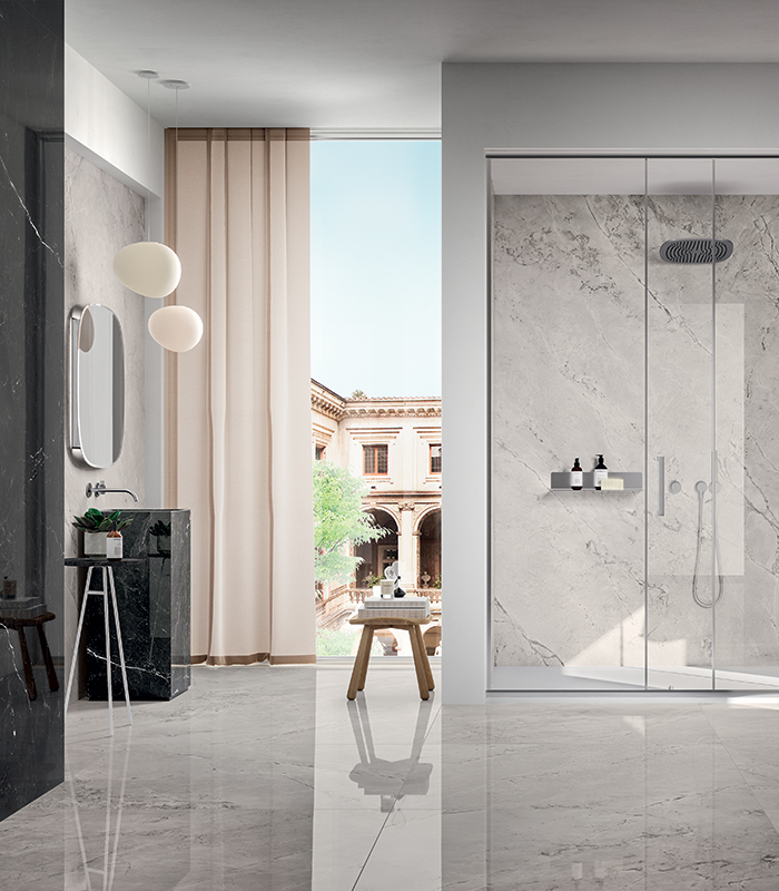 Elegante e luminosa stanza da bagno con pavimento e pareti, inclusa un'ampia doccia, rivestiti in gres porcellanato effetto marmo bianco. Sulla sinistra si scorge una parte rivestita in gres look marmo nero, come pure il lavabo freestanding.