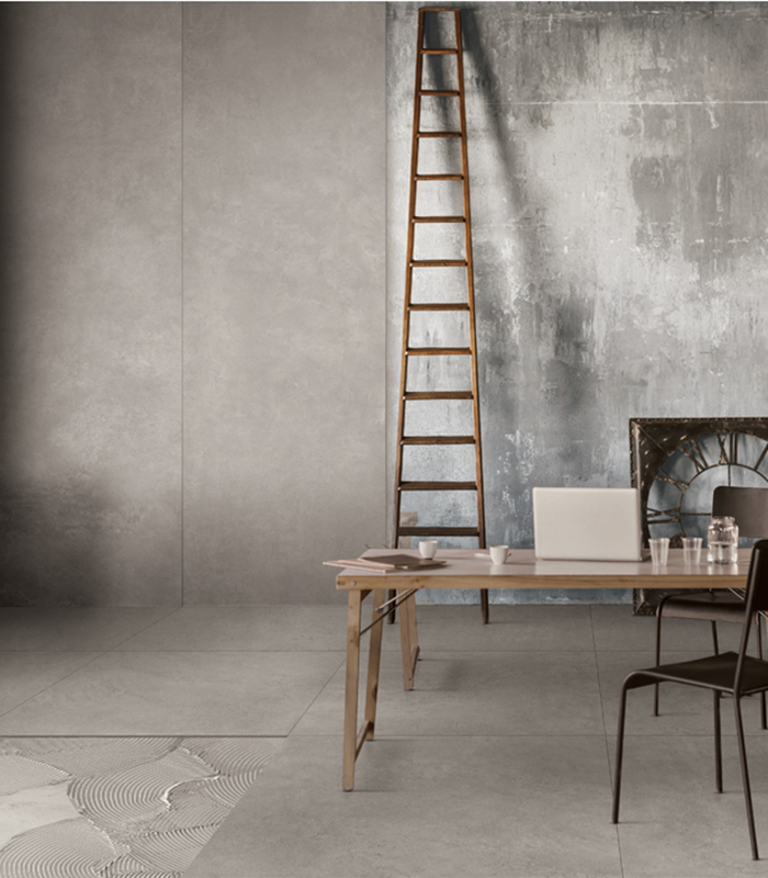 Spazio ufficio in stile industriale con pavimento effetto cemento, pareti materiche, scala in legno e arredi minimal in legno e metallo.