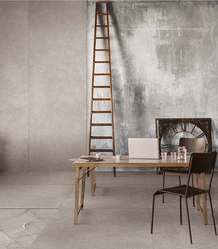 Spazio ufficio in stile industriale con pavimento effetto cemento, pareti materiche, scala in legno e arredi minimal in legno e metallo.