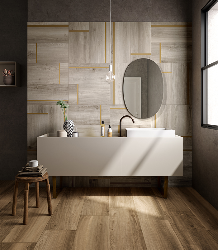 Vista frontale della parete lavabo di un bagno moderno, con pavimento in doghe di legno ceramico e rivestimento in gres porcellanato decorativo effetto legno con l'inserimento di listelli di ottone.