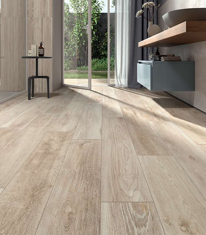 Vista quasi rasoterra di un pavimento in gres porcellanato effetto legno. Le doghe ceramiche guidano lo sguardo verso il resto della stanza: un moderno e luminoso bagno domestico. Collezione Kairos di Panaria Ceramica.