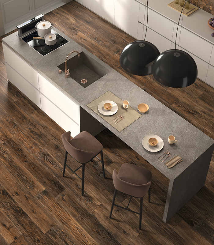 Vista dall'alto di una cucina moderna con isola dinette rivestita con lastre di gres effetto pietra color grigio chiaro e con pavimento in doghe scure di gres porcellanato effetto legno