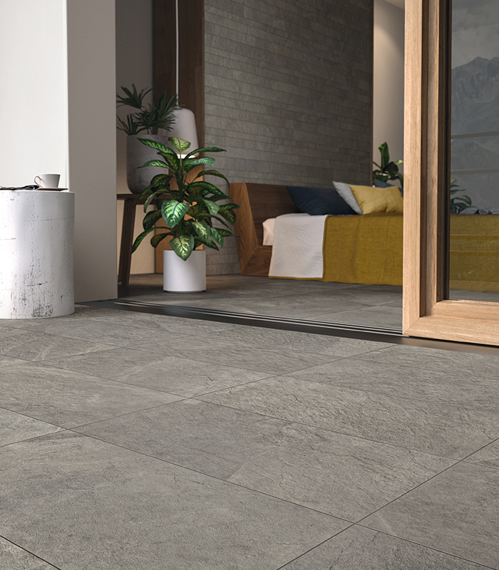 Vista raso pavimento di pavimentazione esterna e porta finestra di una stanza da letto. Pavimenti esterno e interno abbinati tra loro, in gres porcellanato effetto pietra di colore grigio