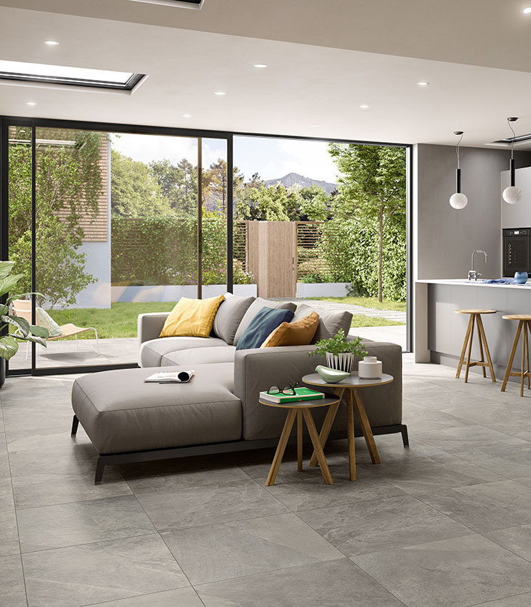 Vista di openspace living-cucina con grande porta vetrata che affaccia su un piccolo giardino privato. Pavimento in gres porcellanato effetto pietra grigio