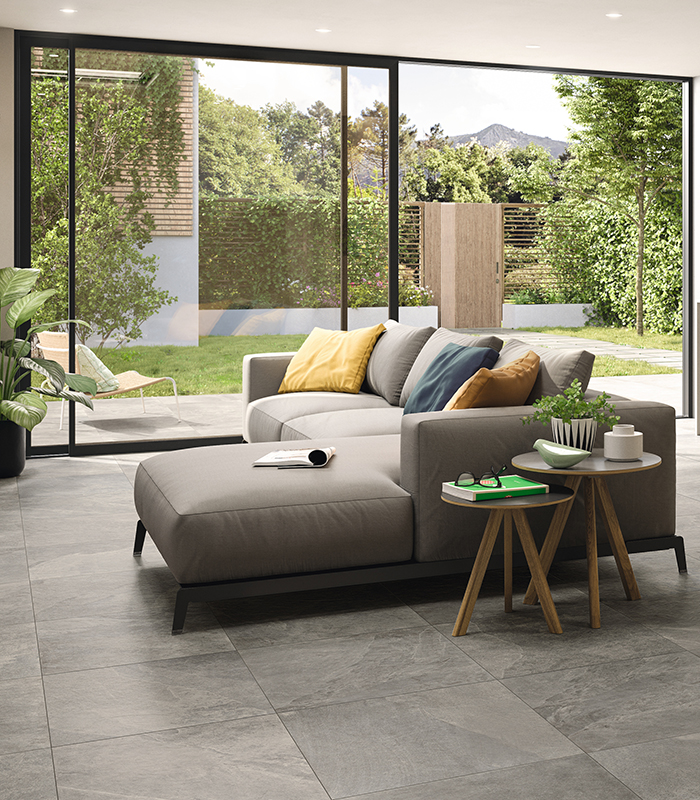 Vista di openspace living-cucina con grande porta vetrata che affaccia su un piccolo giardino privato. Pavimento in gres porcellanato effetto pietra grigio