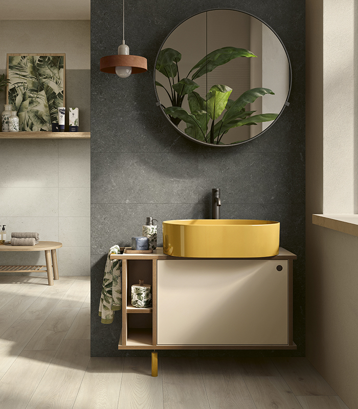 Piccolo bagno domestico con pavimento in gres effetto legno chiaro e rivestimento in ceramica effetto pietra scura, lavabo in ceramica gialla e specchio rotondo