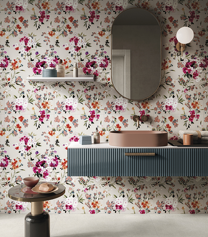 Veduta frontale della parete lavabo di un bagno pavimentato con gres porcellanato effetto cemento di colore chiaro e rivestimento in lastre sottili di gres effetto wallpaper con motivo floreale