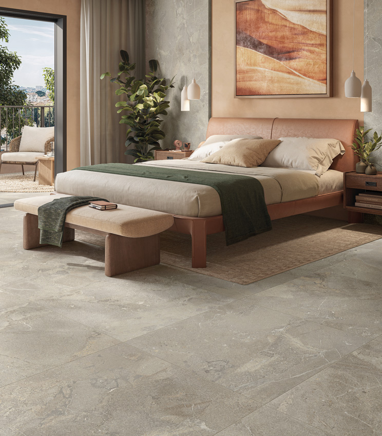 Luminosa stanza da letto con pavimento e rivestimento effetto pietra beige, grande quadro con paesaggio astratto sulla parete del letto e scorcio di terrazzo sulla sinistra.