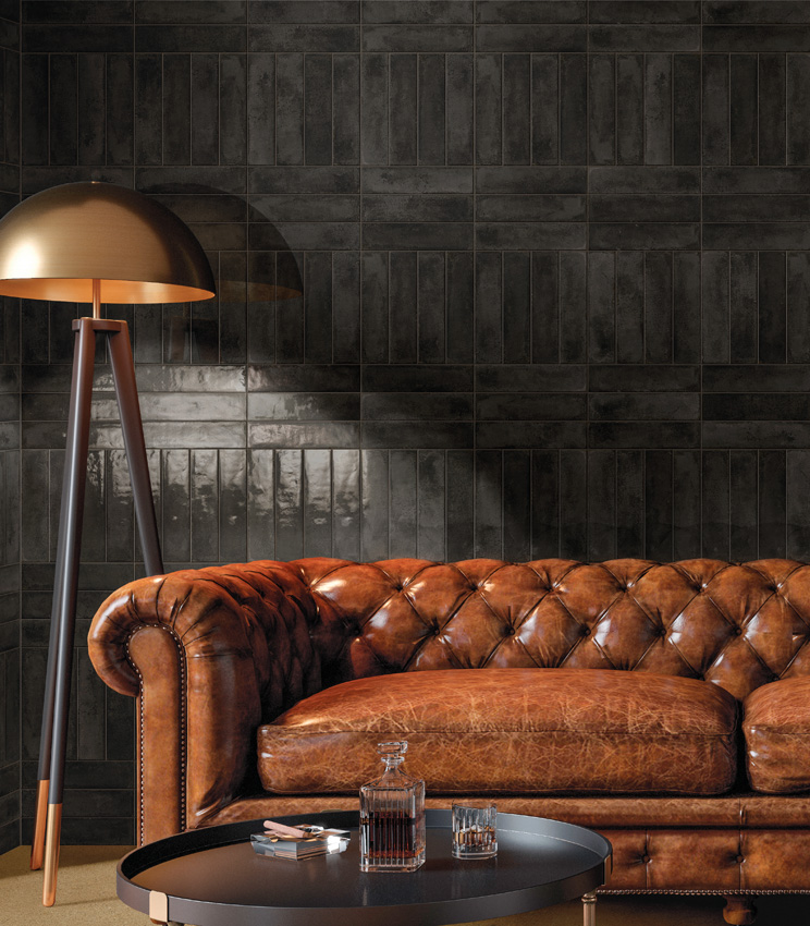 Scorcio frontale di living con parete rivestita con mattoncini ceramici smaltati lucidi di colore nero e grande divano Chesterfield con lampada da terra a treppiede.