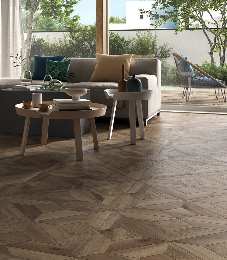 Scorcio di living con ampia vetrata e due grandi divani, con pavimento in gres porcellanato effetto legno di colore scuro che reinterpreta la posa a cassettone.