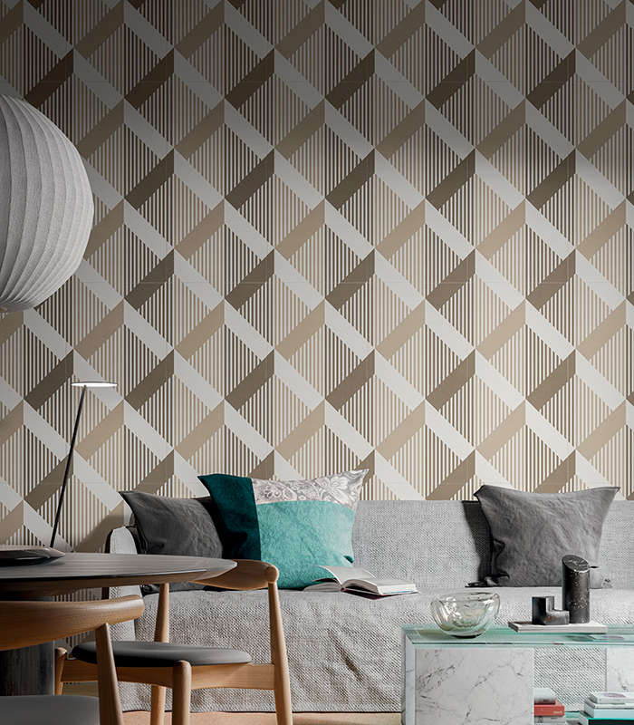 Scorcio di living minimalista ma accogliente con tavolo tondo sulla sinistra e divano grigio chiaro sullo sfondo. Protagonista è la parete alle spalle del divano, rivestita con lastre di gres effetto wallpaper dalla raffinata texture geometrica.