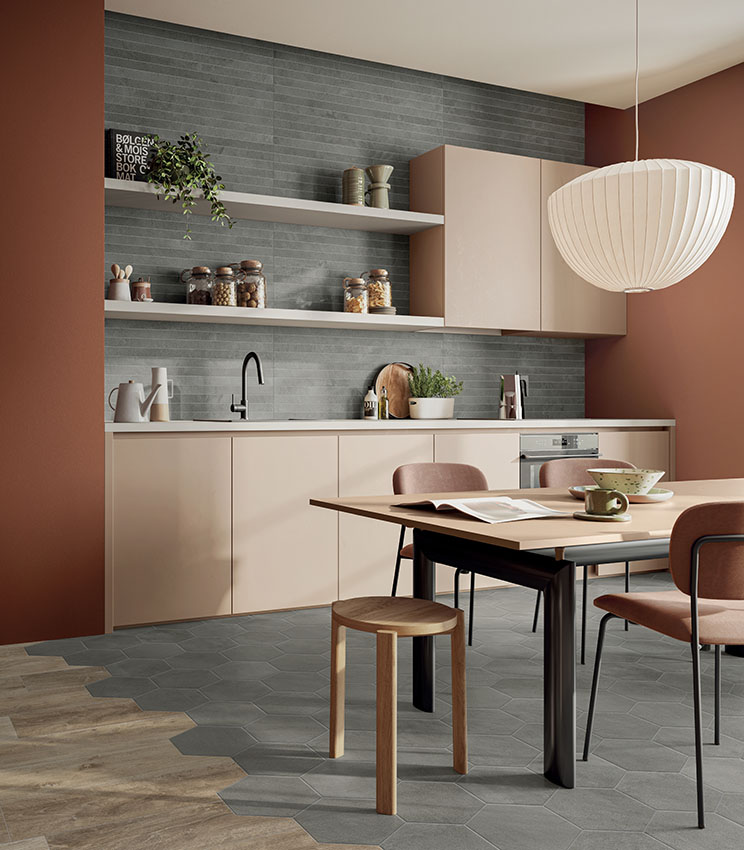 Cucina contemporanea con rivestimento grigio a listelli e pavimento geometrico, arredata con mobili beige, pareti color terracotta, tavolo da pranzo con sedie imbottite e una grande lampada a sospensione bianca.