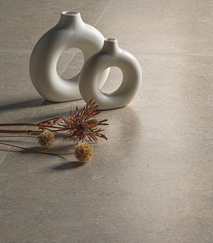 Dettaglio di pavimento della collezione Surround Row Soft, in tonalità beige effetto pietra, decorato con due vasi scultorei chiari e composizioni di fiori secchi.