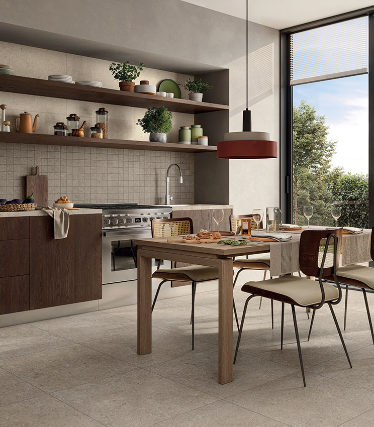 Cucina moderna con pavimento e rivestimento in piastrelle beige effetto pietra, arredi in legno, tavolo da pranzo e ampia finestra.