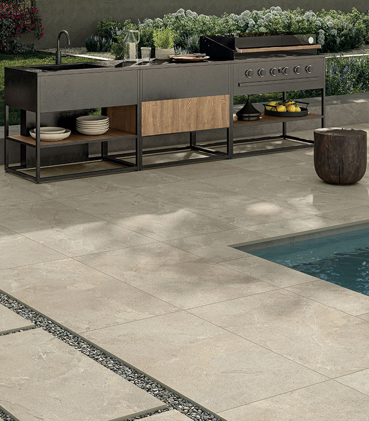 Area piscina con pavimentazione in gres porcellanato effetto pietra, cucina outdoor e arredi contemporanei, per uno spazio elegante, resistente e funzionale.