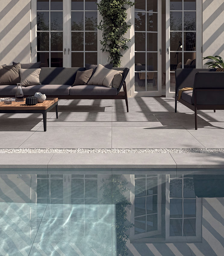 Area piscina con pavimentazione in gres porcellanato effetto cemento, arredi outdoor contemporanei e ampie vetrate, per uno spazio elegante e funzionale.
